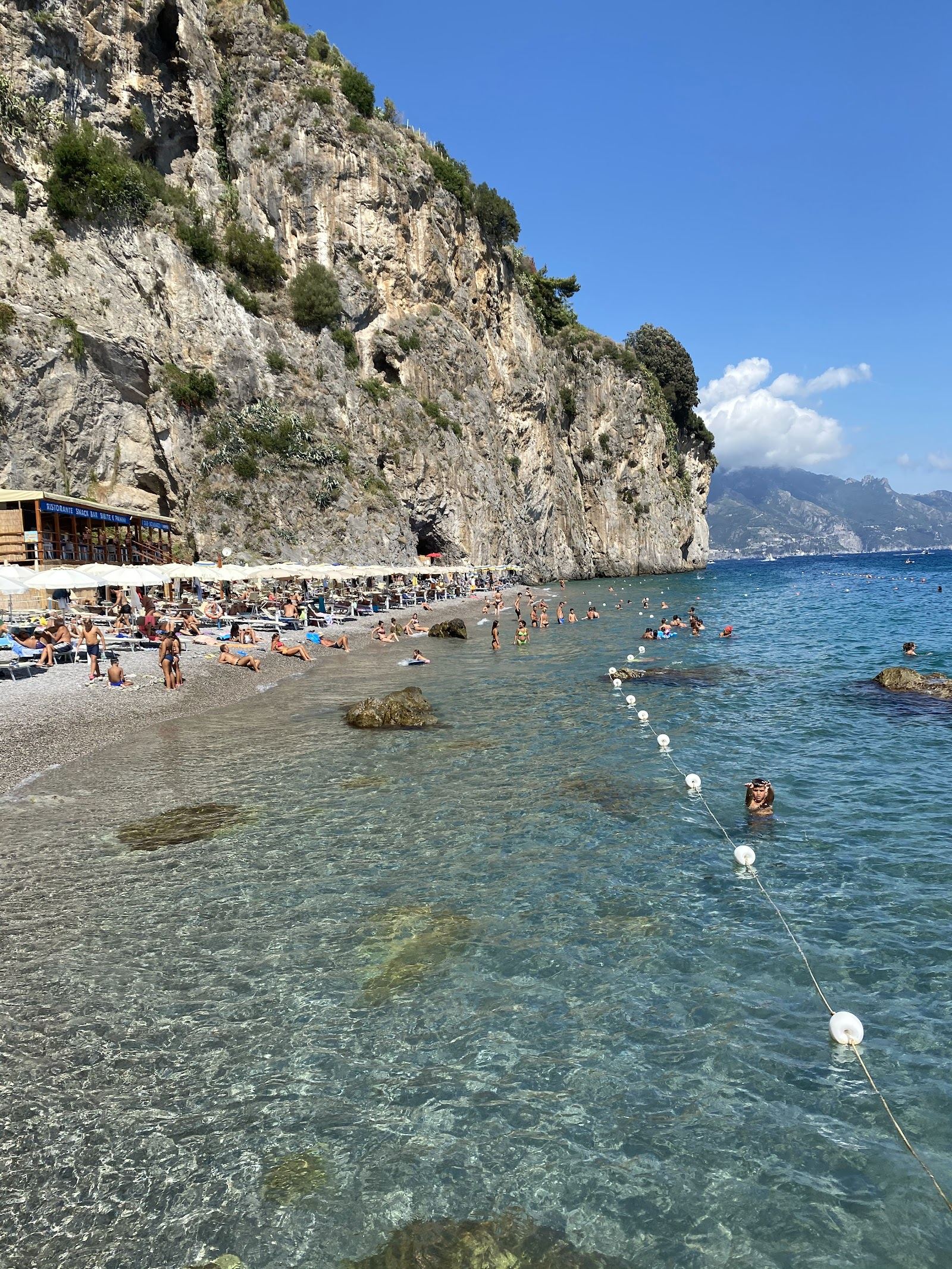 Clear blue water over pale grey pebbles at Duoglio cove below the cliffs near Amalfi town