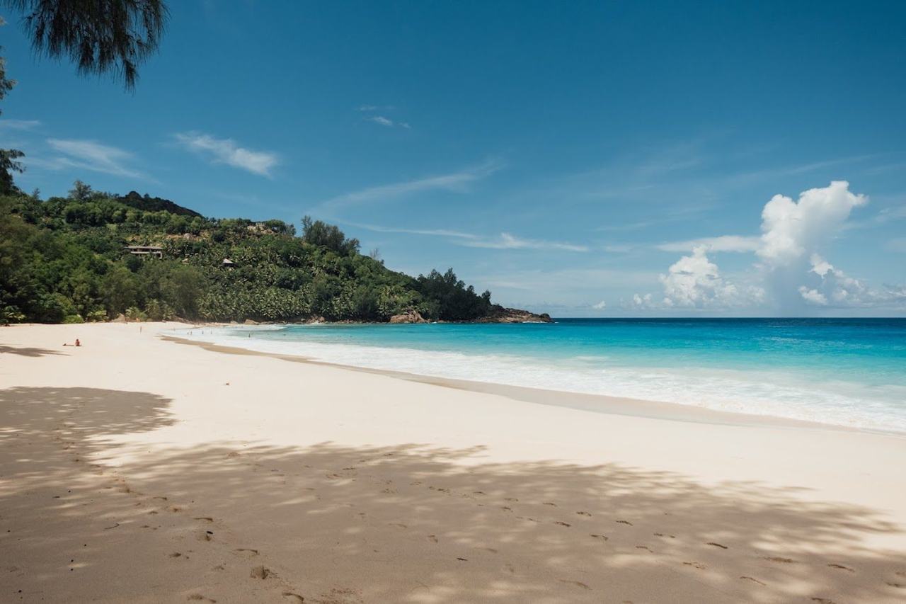 Wide empty white sand beach with rolling surf and forested headland at Anse Intendance on south Mahe