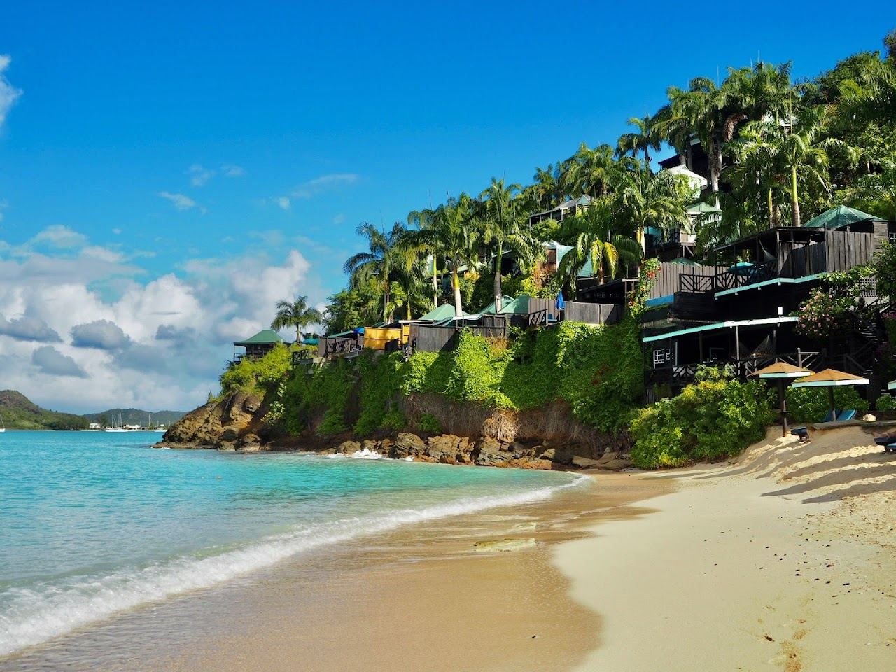 Wide sweep of white sand and calm clear shallow water in bright light at Valley Church Beach in Antigua