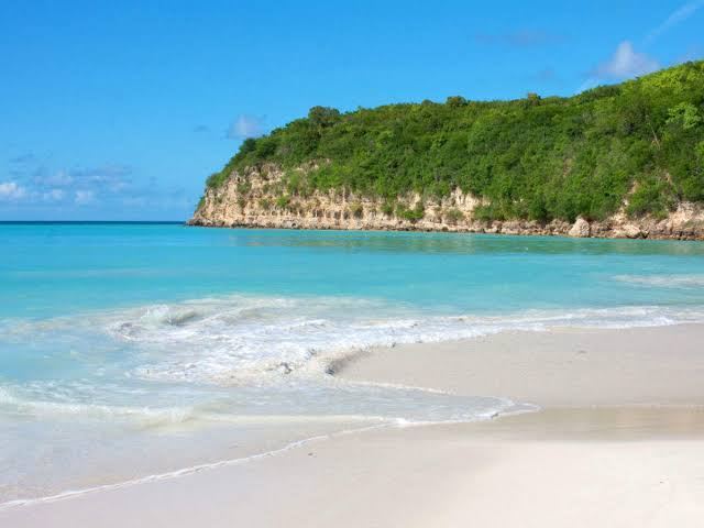 A calm turquoise Antigua bay with watersports operators along a wide sandy beach