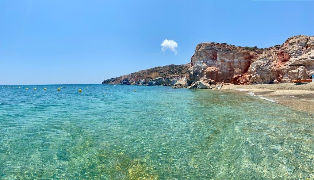Clear water and red streaked cliffs along the volcanic sand of Paliochori beach on the south coast of Milos