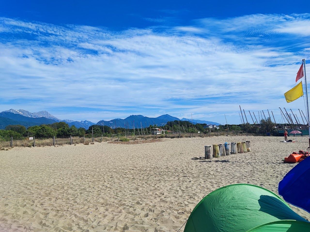 The wide flat sand of Forte dei Marmi beach with umbrella rows and the Apuan Alps rising inland