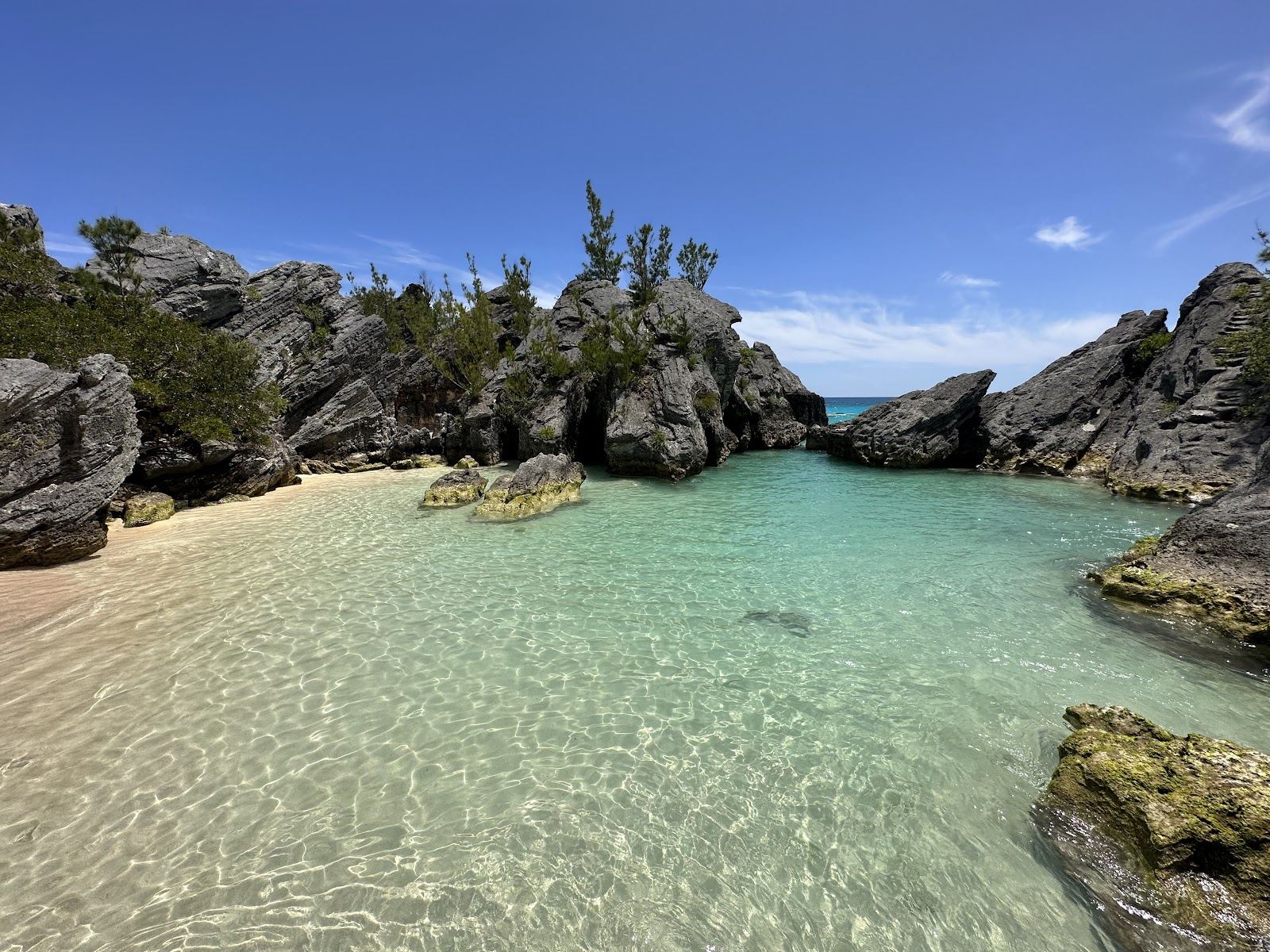 A small hidden cove of pink sand and clear turquoise water ringed by rock on the south shore of Bermuda