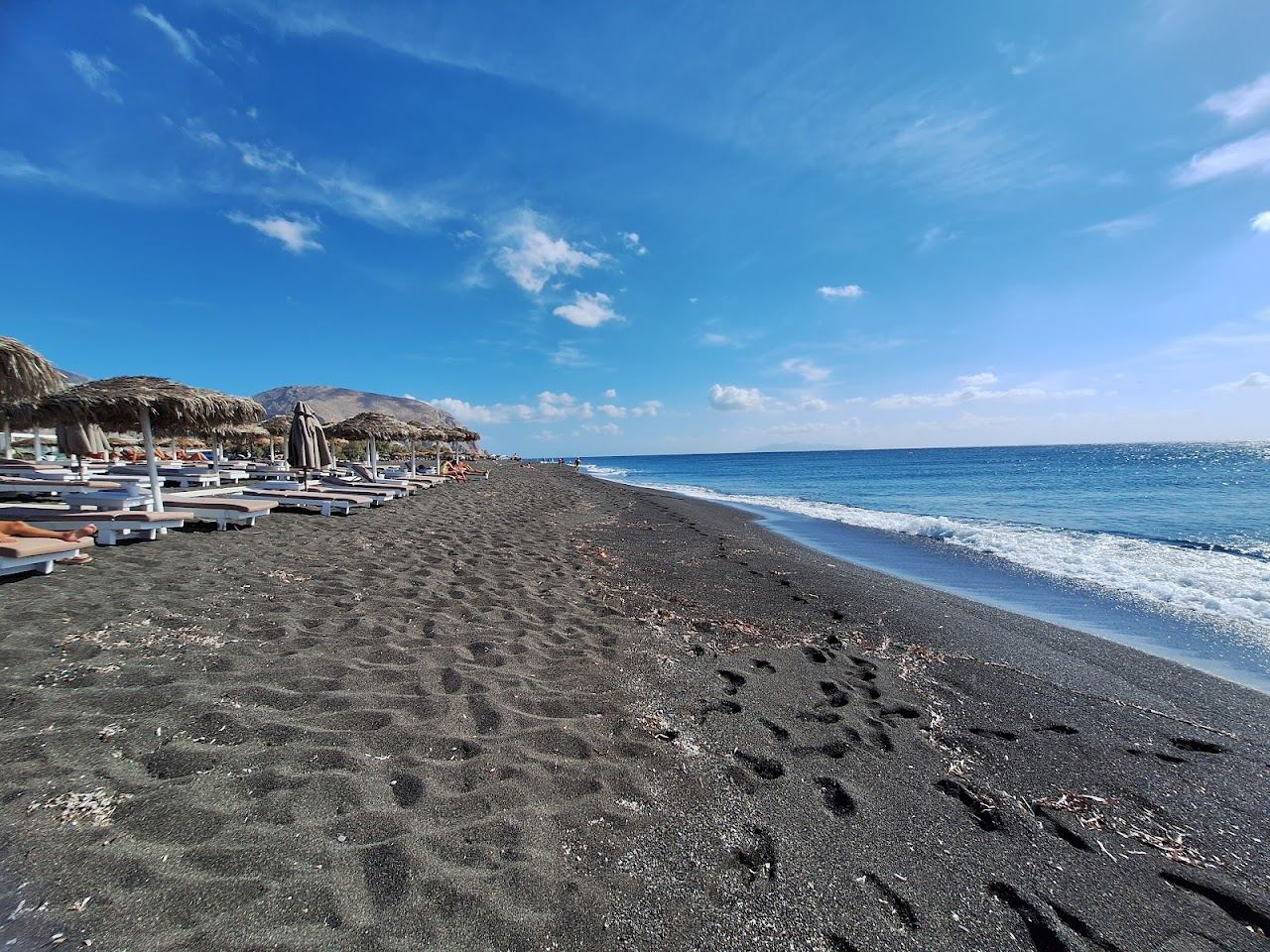 Black volcanic sand and sea facing loungers at Perivolos on Santorini