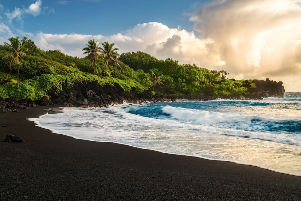 A jewel box cove of black sand framed by green jungle, lava caves and blowholes on the road to Hana.