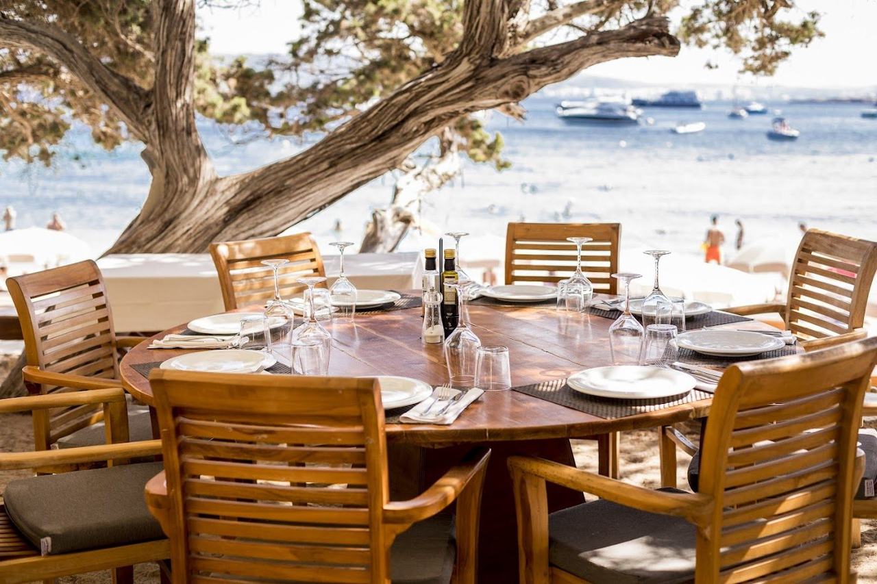 Sunbeds on the white sand of Cala Bassa with the beach club and pines behind in western Ibiza