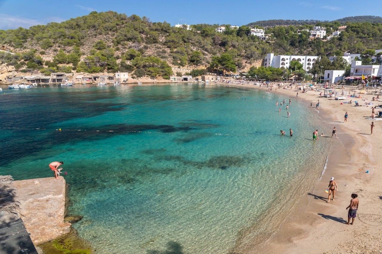 The sheltered horseshoe bay of Cala Vadella with fine sand and calm water below a hillside of villas in west Ibiza
