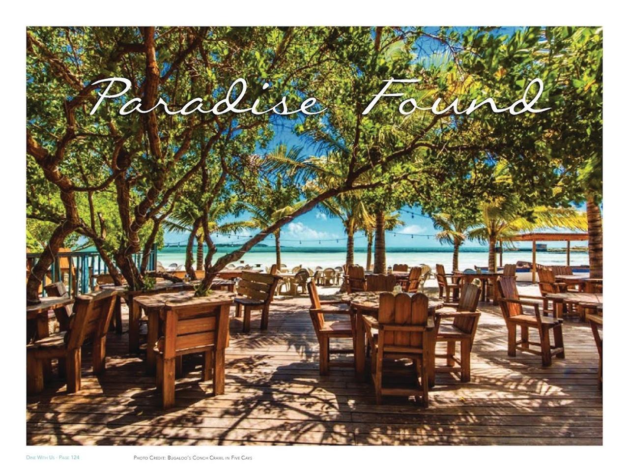Tables on the sand under palms beside the shallow water at Bugaloos on Five Cays beach