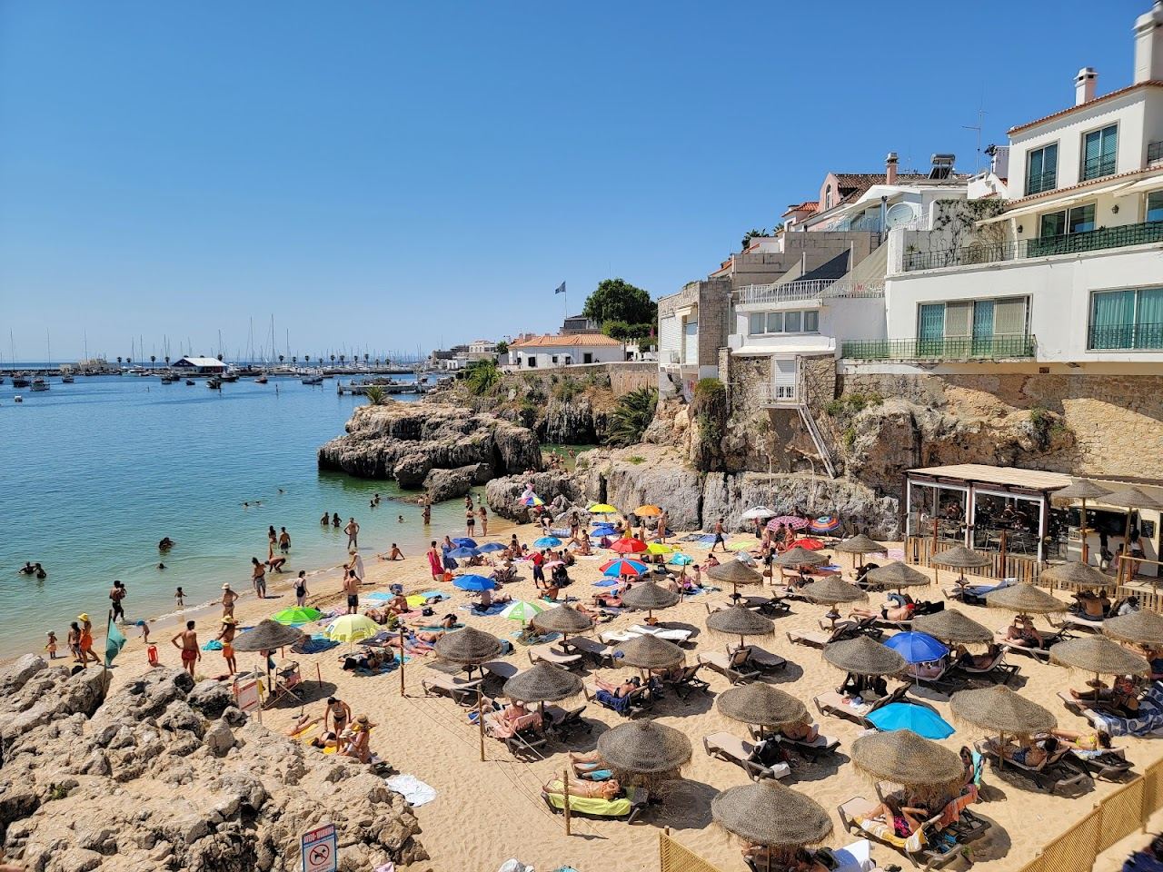 Small golden cove sheltered by rock below the town at Praia da Rainha in Cascais