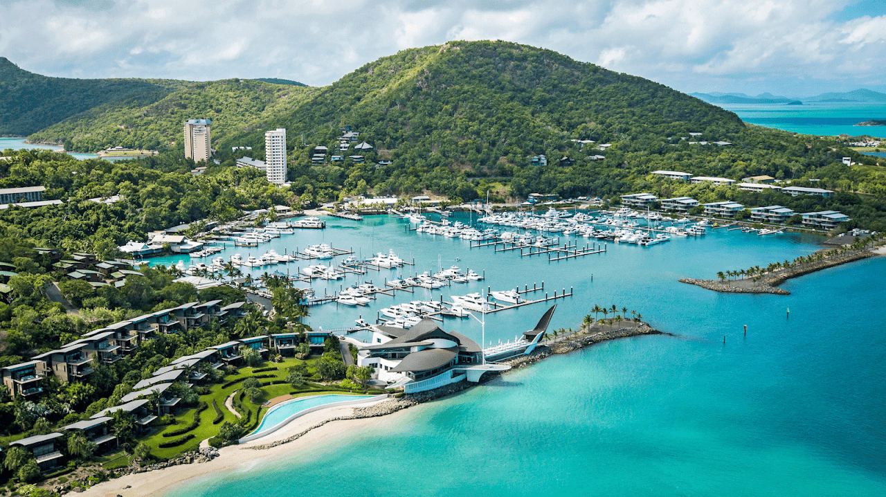 Beach and marina with boats and green hills on Hamilton Island in the Whitsundays