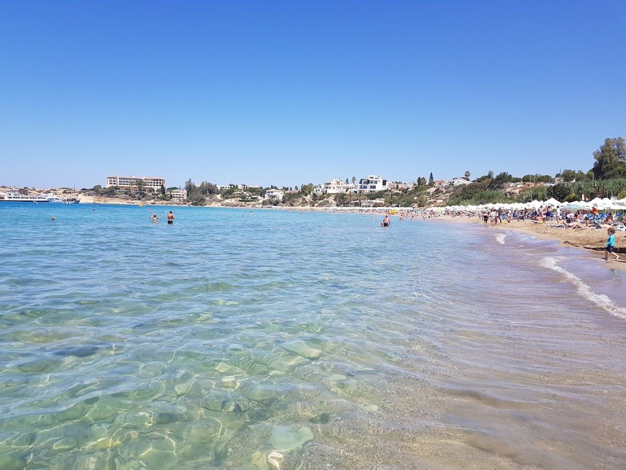 Sheltered curve of golden sand and calm shallow water between two headlands at Coral Bay near Paphos Cyprus