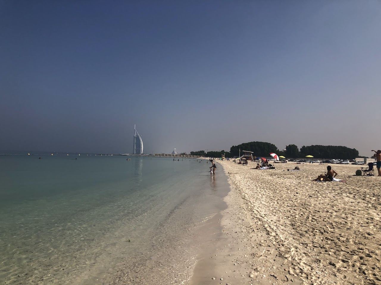 Pale groomed sand and calm Gulf water at a quiet public beach in Dubai with city towers in the distance
