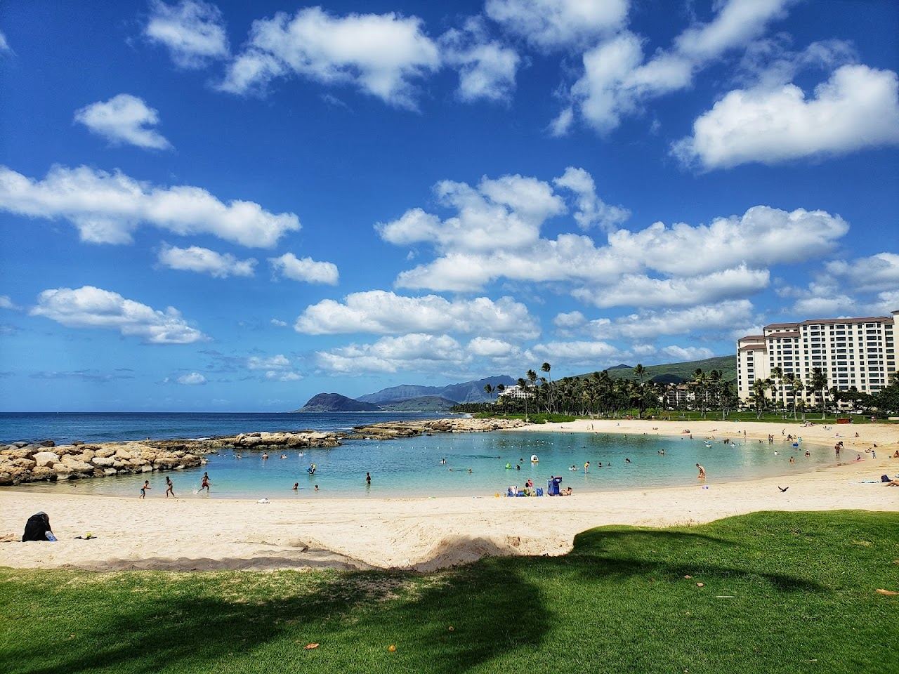 The walled calm water of a Ko Olina lagoon with grass and palms behind