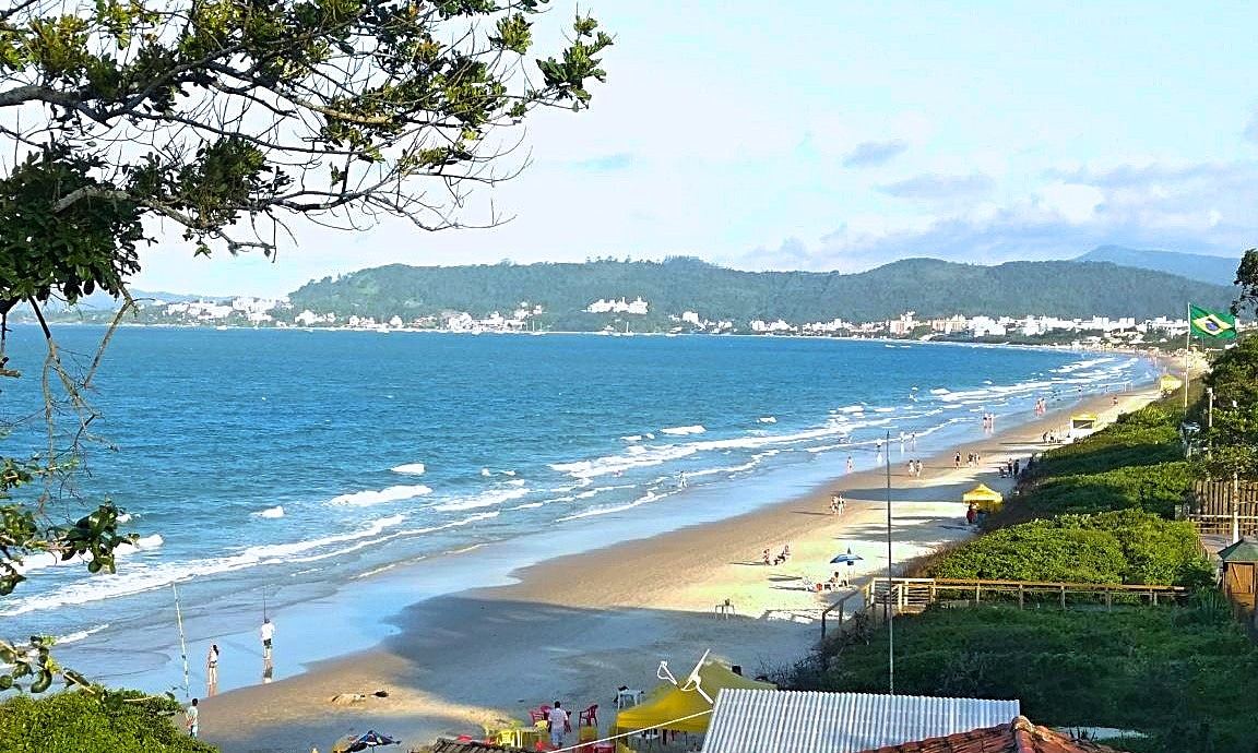 A wide sweep of sand and a lively summer crowd at a party beach in Florianopolis.