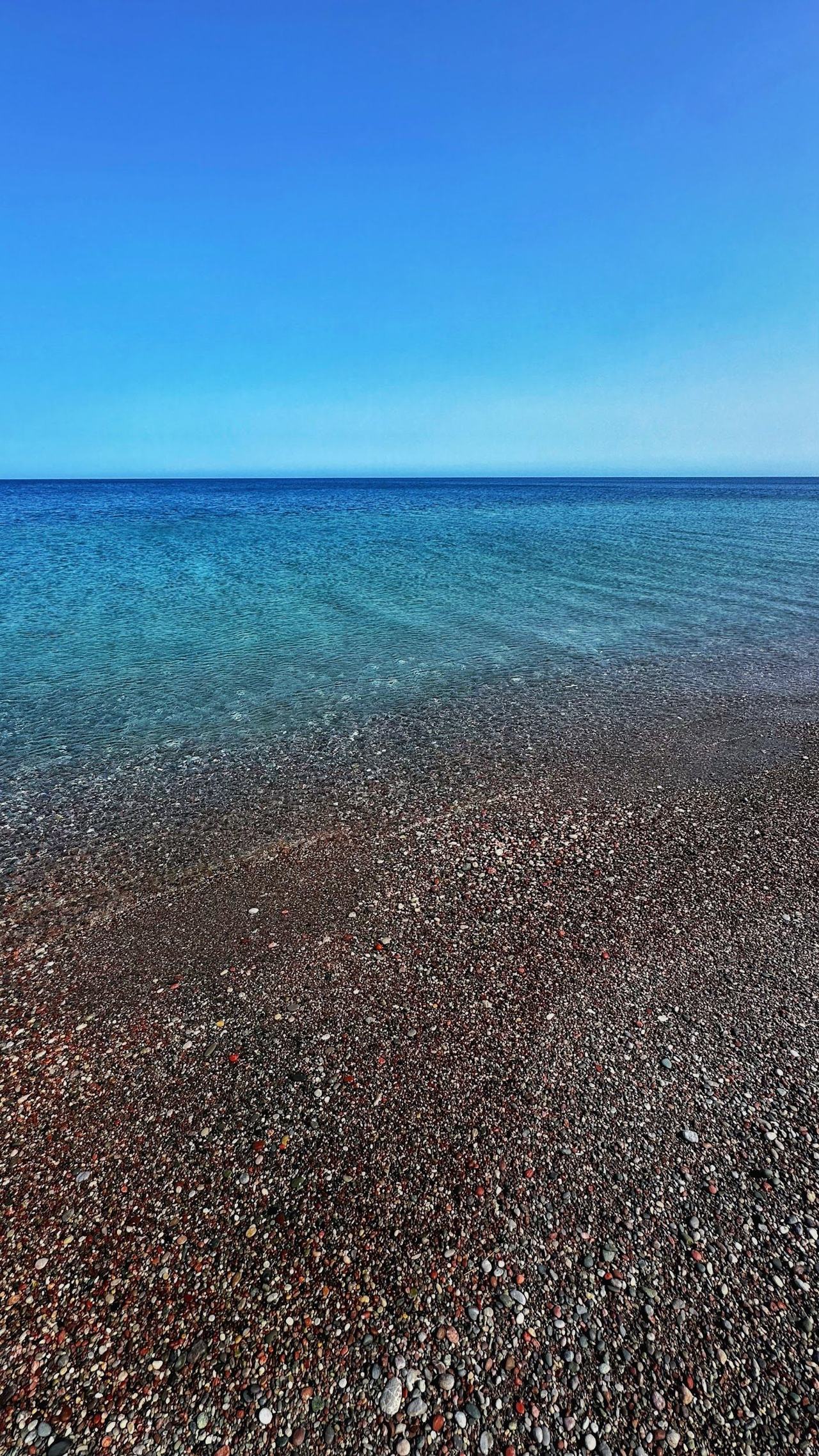 The long open pebble shore and clear sea of Gennadi beach stretching away with low scrub behind on the southeast coast of Rhodes