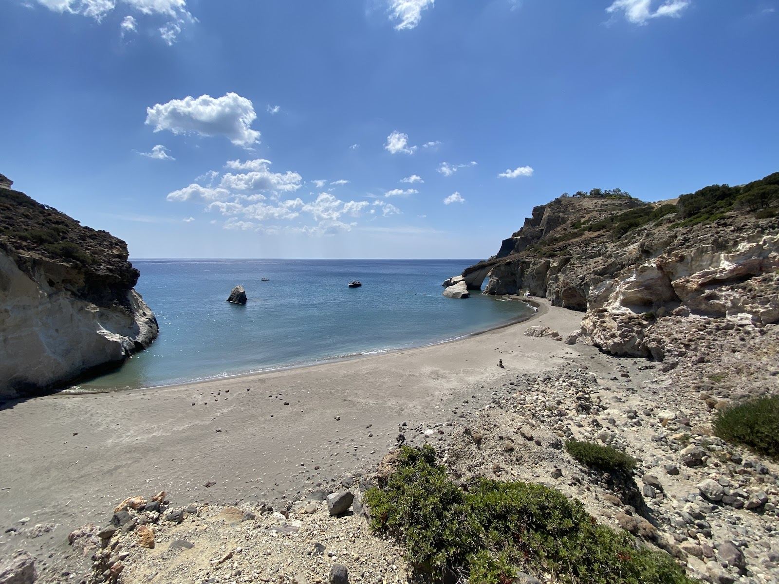 The remote beach at Gerontas with white cliffs, dark sand and a rock arch in the clear sea on the south coast of Milos