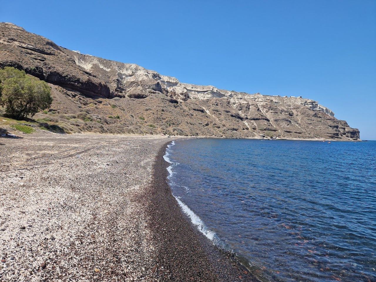 The sheltered dark sand cove of Gialos below Akrotiri with calm water and caldera views in Santorini