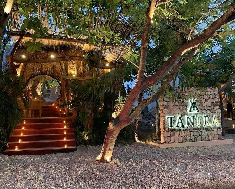 A boho beach club of palms and daybeds where groups gather on the sand in Tulum
