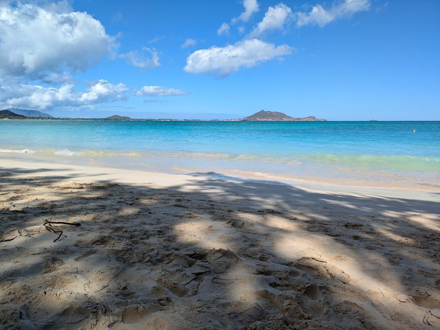 The wide pale sand and bright blue water of Kailua Beach with windsurfers offshore on Oahu