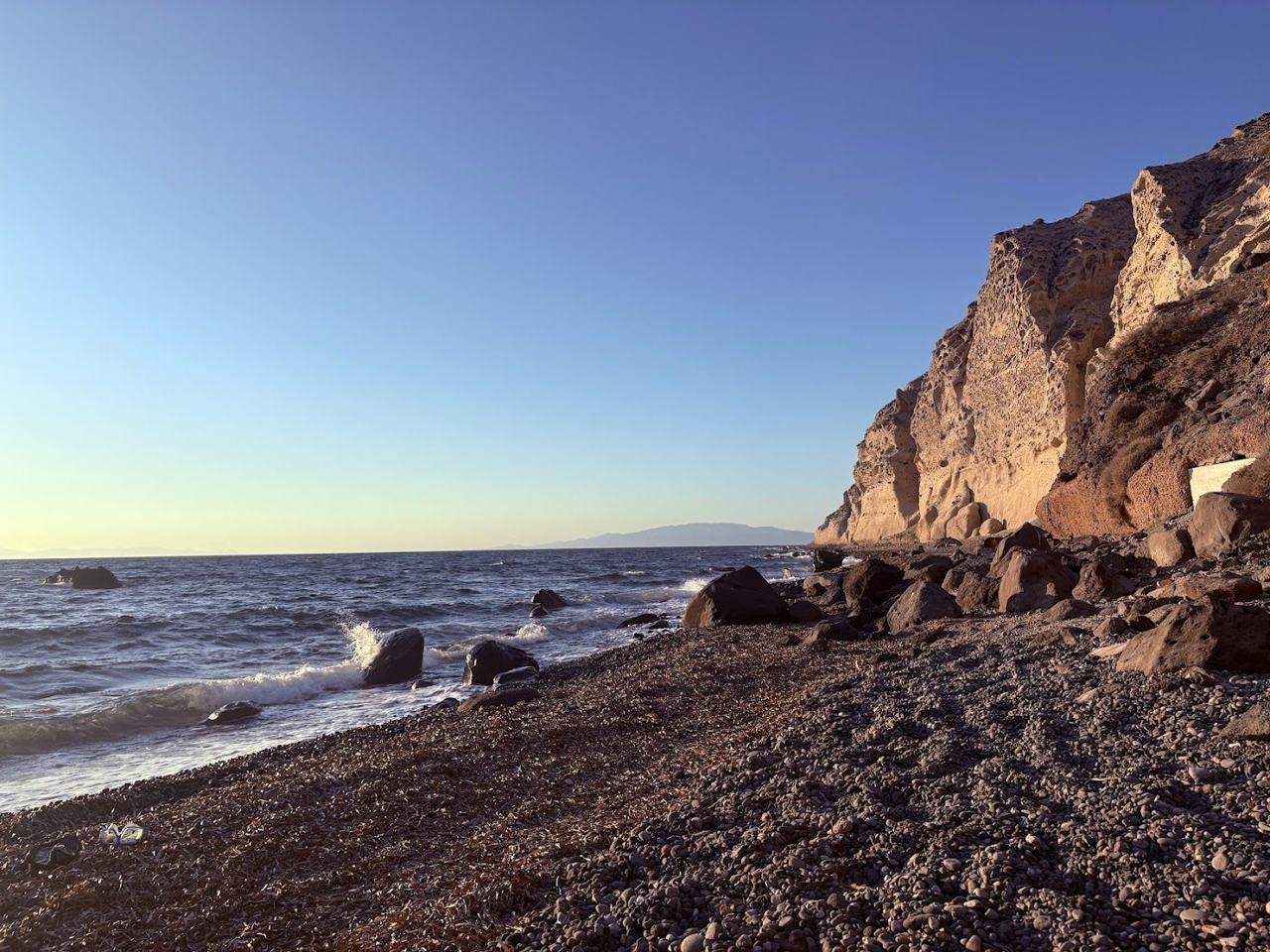 The dark gravel and dramatic volcanic cliffs of Katharos Beach below Oia in northern Santorini