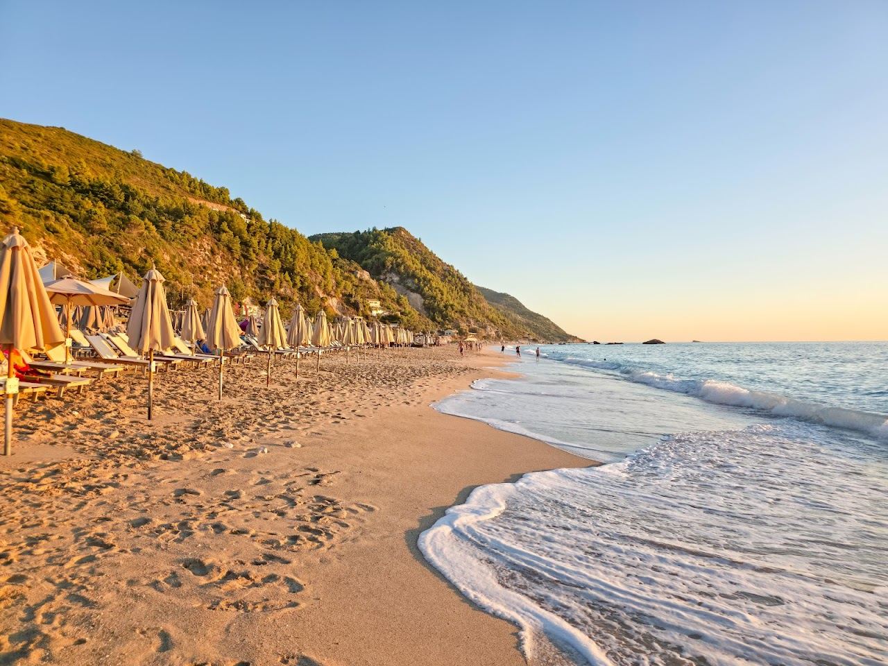 A long open sweep of pale sand meeting clear blue water with sunbeds and beach bars at Kathisma beach on the west coast of Lefkada