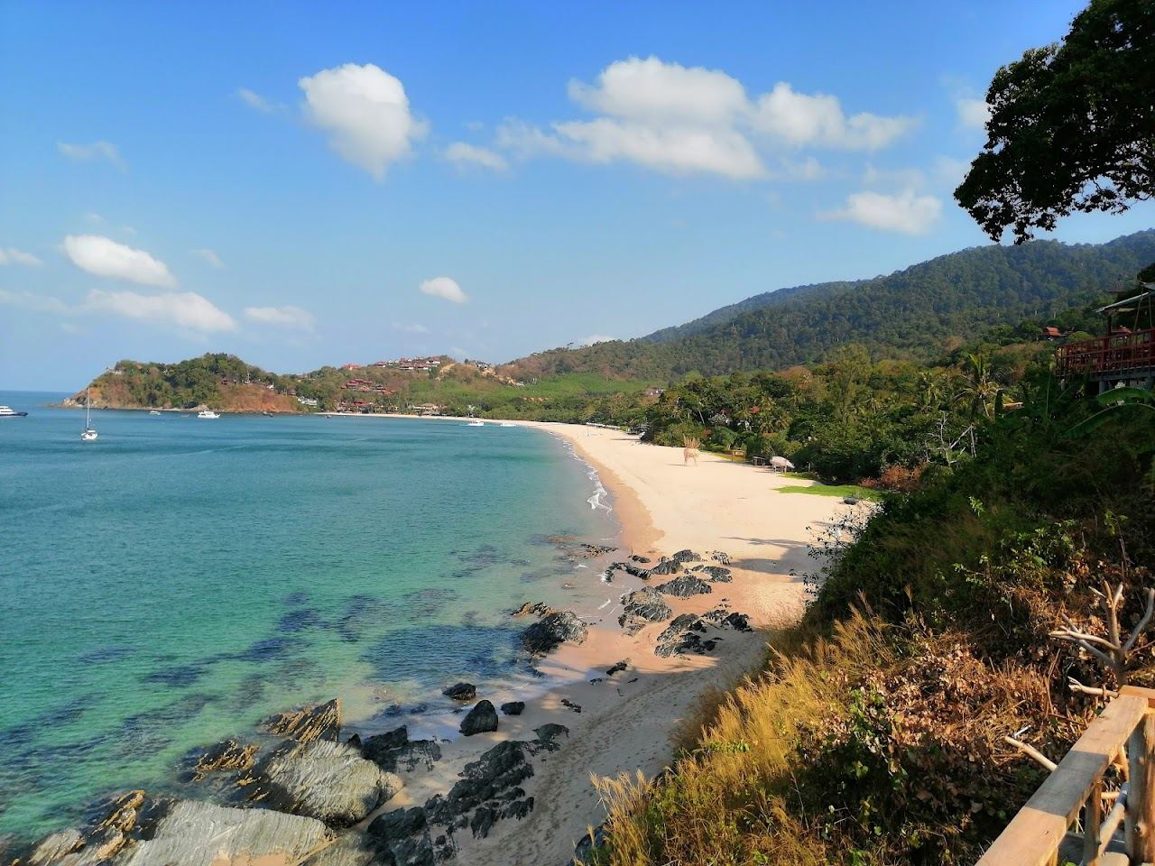 Calm turquoise Andaman Sea water and a quiet sandy bay backed by green hills on Koh Lanta in Thailand