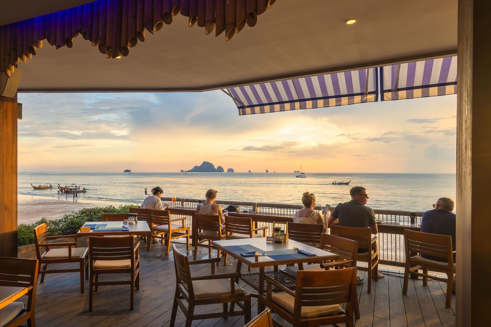 Loungers on Ao Nang sand facing the Andaman Sea at a Krabi beach club near sunset