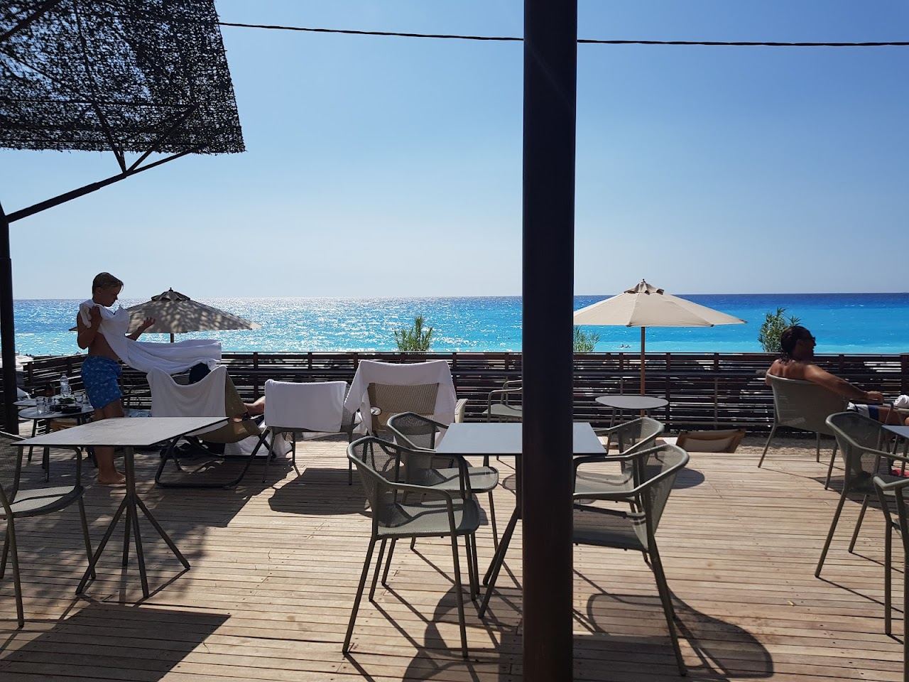 A lively west coast beach with bars and loungers above pale sand and clear water in Lefkada