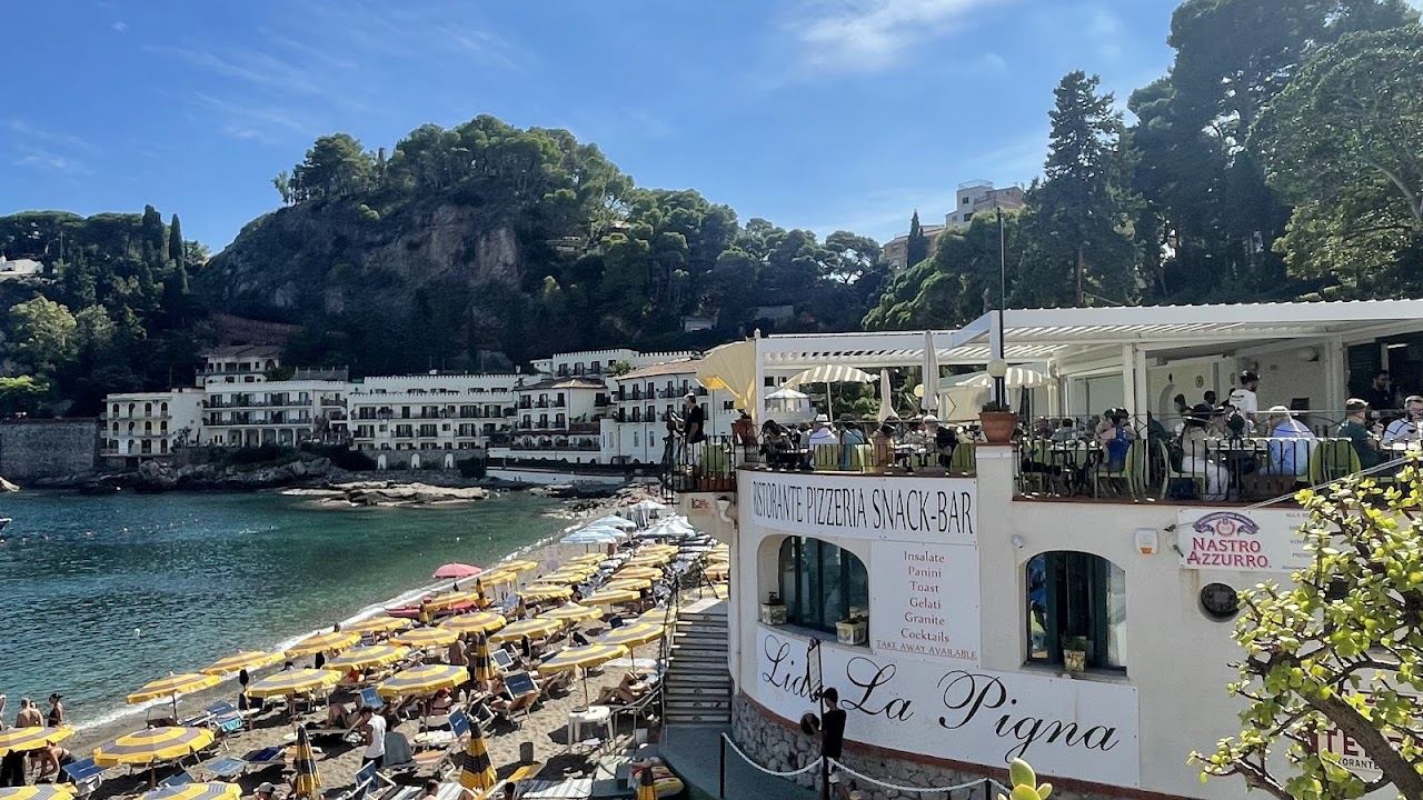 Turquoise water over pale pebbles at Mazzaro bay with umbrella rows and green headlands, Taormina
