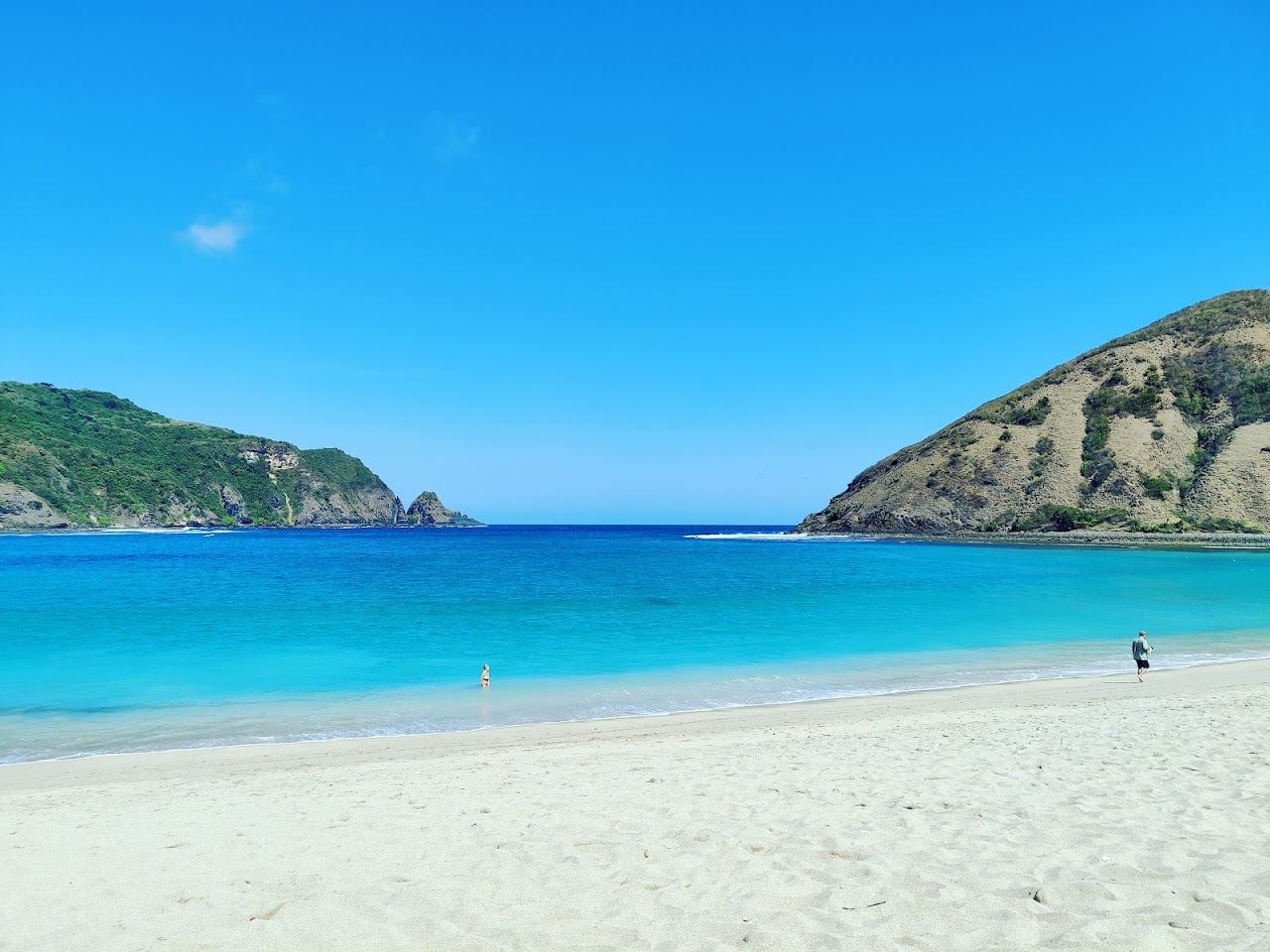 A calm horseshoe bay of pale sand framed by green headlands on the south coast of Lombok