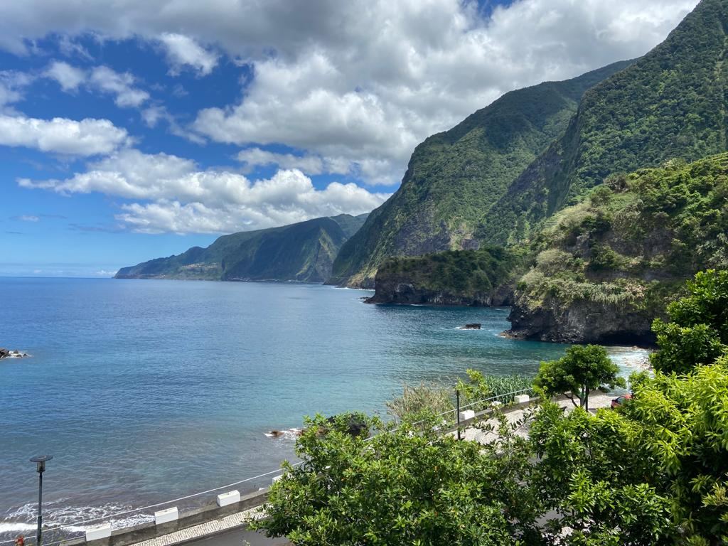 Black volcanic sand meeting turquoise water below steep green cliffs at Seixal on the wild north coast of Madeira