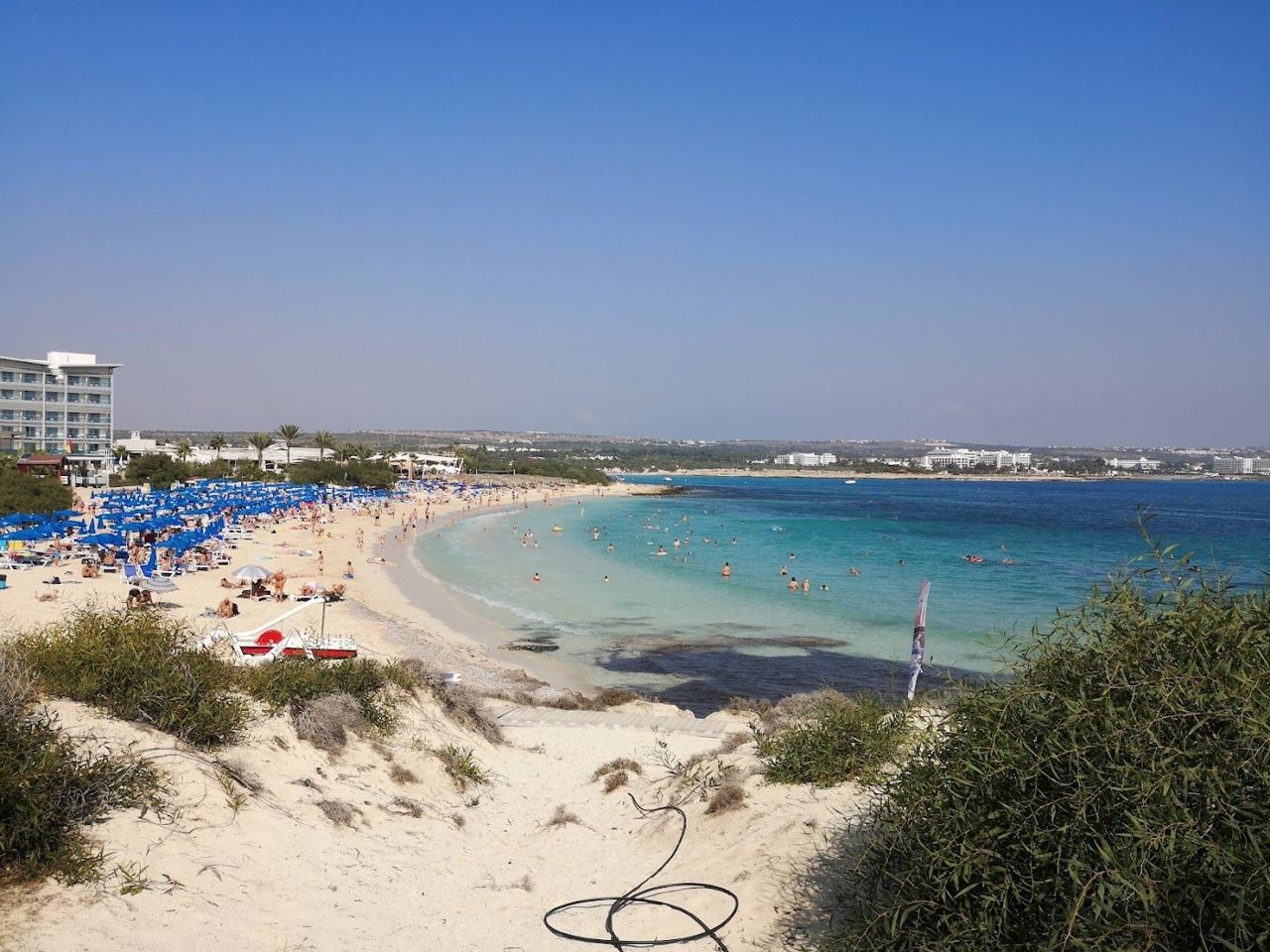 Linked sandy coves and calm shallow turquoise water with sunbeds at Makronissos beach near Ayia Napa Cyprus