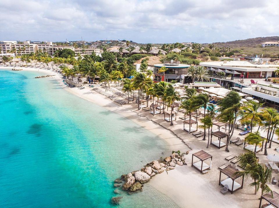Calm sheltered water and pale sand backed by beach bars at Mambo Beach in Curacao