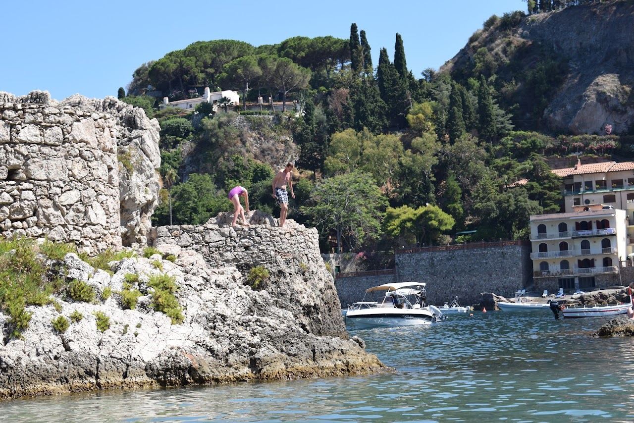 Clear water and pebbles of Mazzaro bay with umbrella rows along the shore below Taormina