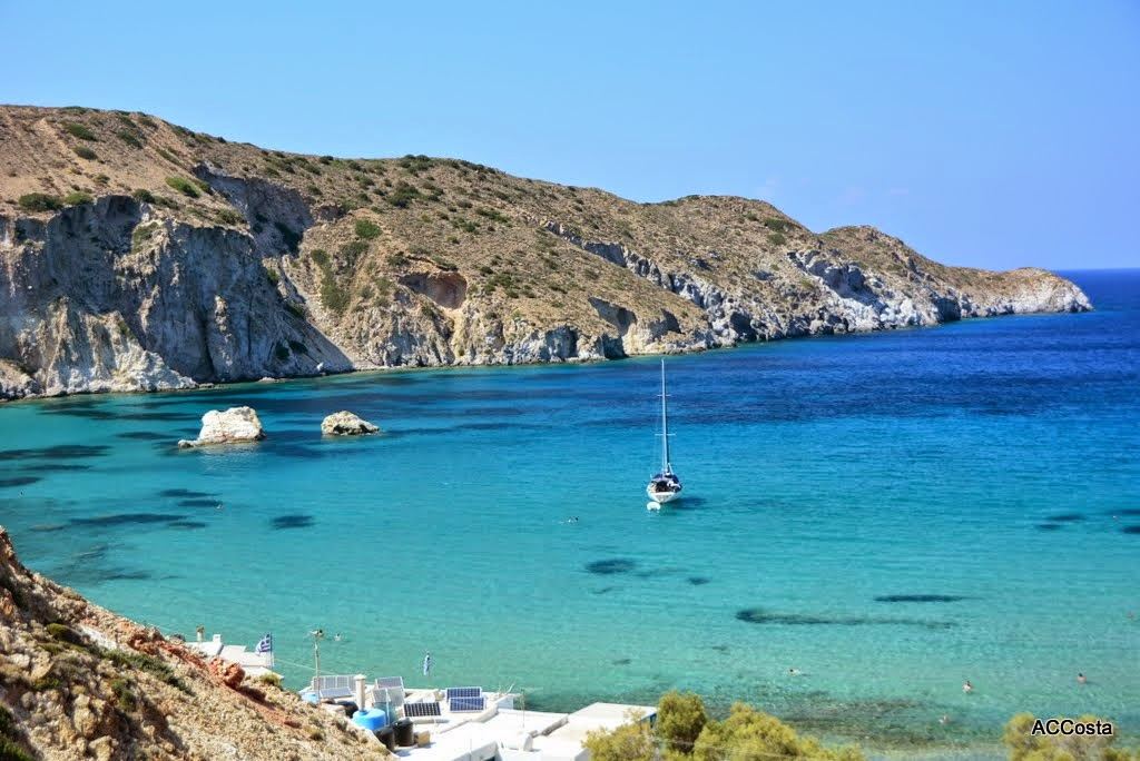 The quiet cove of Firopotamos on Milos with clear calm water below white and blue fishermen boat houses