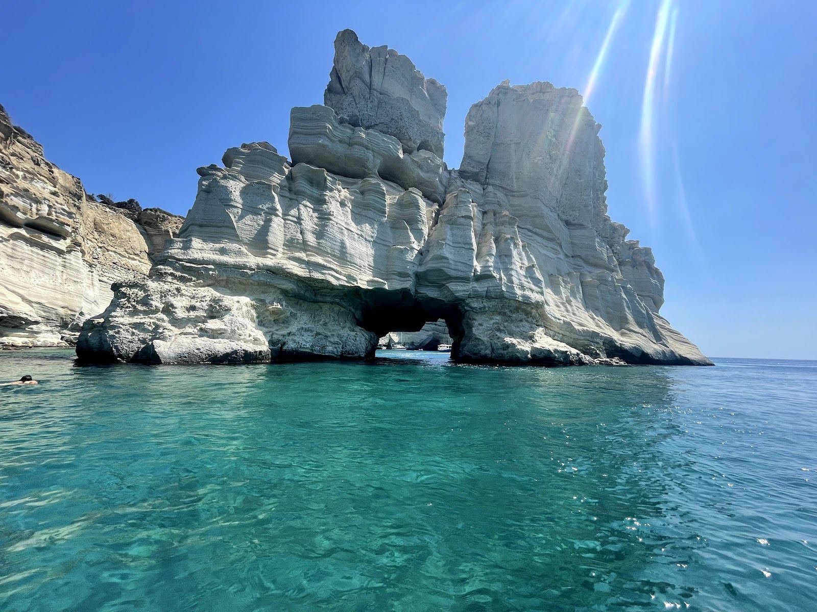 Snorkellers and a small boat in the clear water among the white sea caves and arches of Kleftiko on Milos