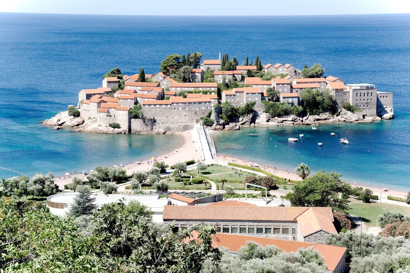 The fortified islet of Sveti Stefan above a calm pink pebble beach on the Montenegro coast