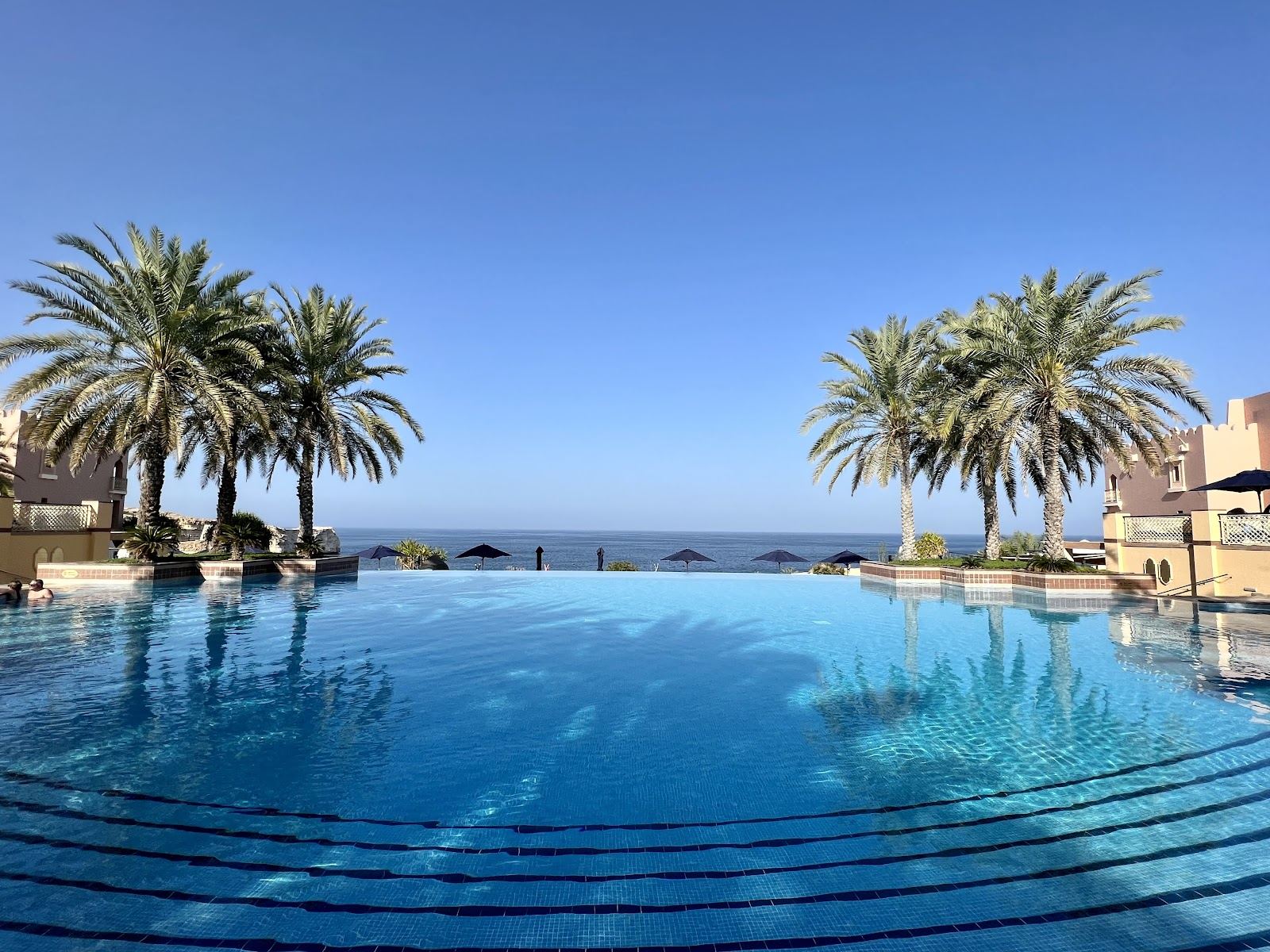 Beach and turquoise bay below rocky mountains at a resort in Muscat, Oman