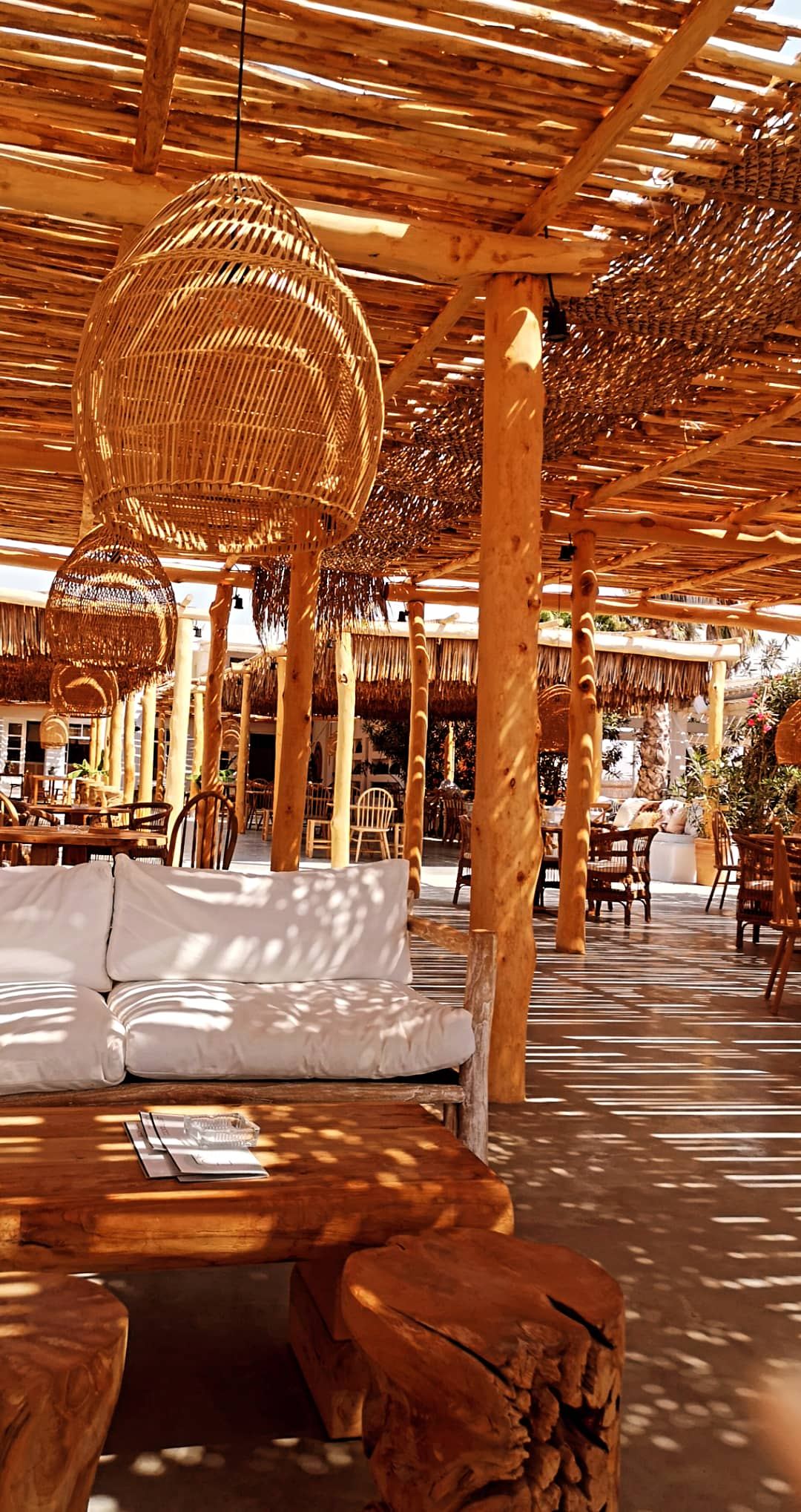 Sunbeds under straw fringed shades in the sand at Nomad beach bar on Plaka beach, Naxos