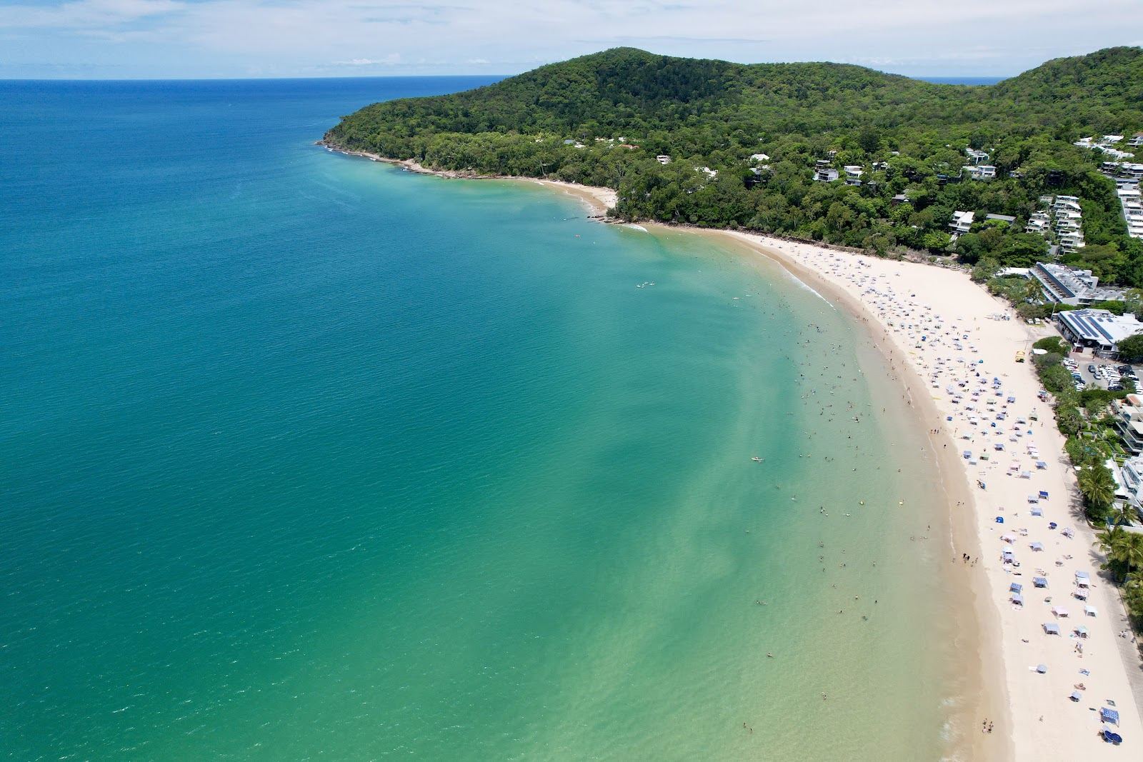 Surfers and paddlers in gentle waves off a golden beach backed by green headland at Noosa in Queensland