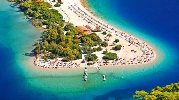 The soft sand spit of the Oludeniz lagoon beach at Kumburnu curving into turquoise water backed by pine hills near Fethiye in Turkey