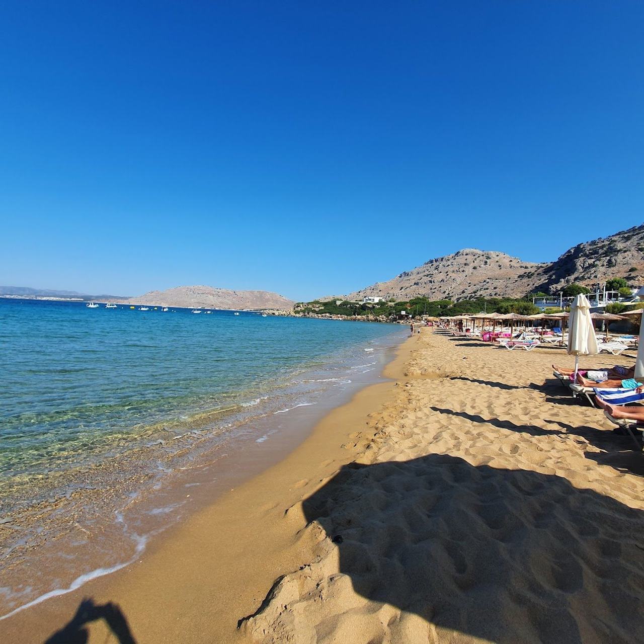 Looking along the small sandy and pebble coves of Pefkos with sunbeds and tavernas behind and clear calm water on the east coast of Rhodes