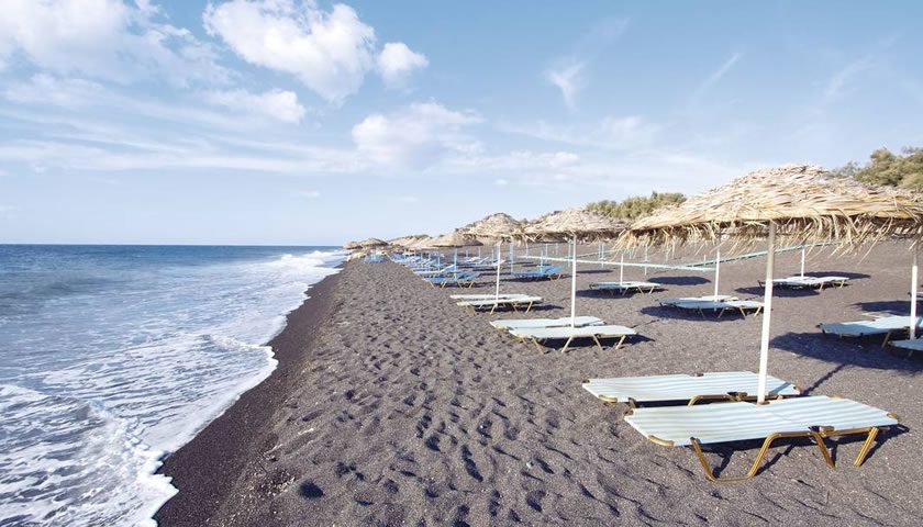 Sunbeds and tavernas along the black sand of Perissa Beach beneath Mesa Vouno on Santorini