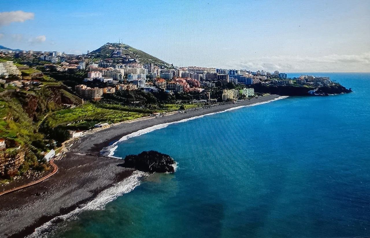 Long curve of dark pebble and black sand along the seafront of Praia Formosa in Funchal, Madeira