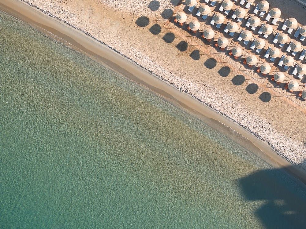 Sunbeds and umbrellas on the golden sand of Provatas beach with a beach bar above the calm shallow water in Milos