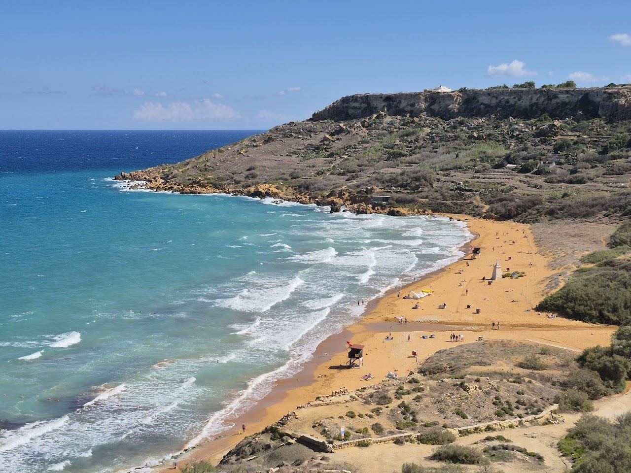 The distinctive red orange sand of Ramla Bay on Gozo below green hills and the Calypso Cave