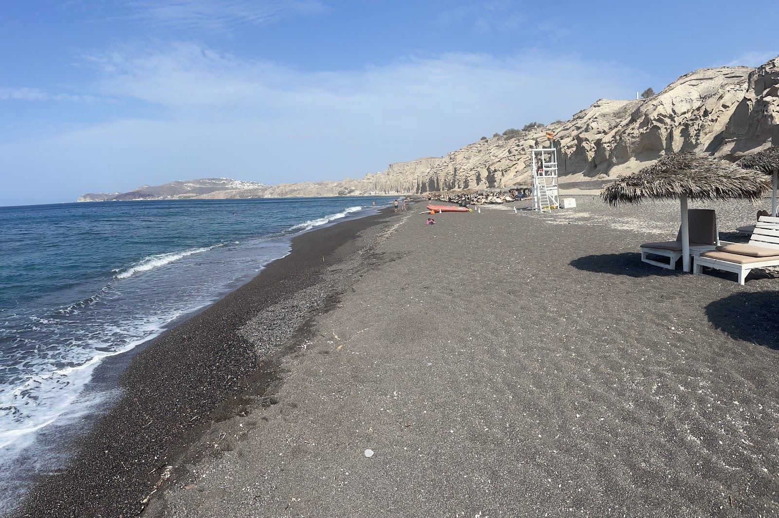 Pale sculpted pumice cliffs above the dark sand and clear water at Vlychada on Santorini