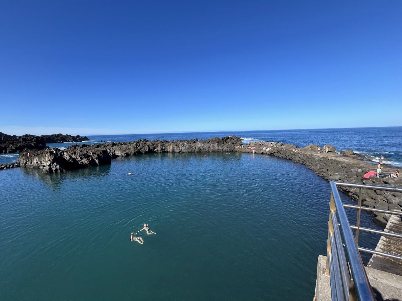 Dramatic black volcanic sand and a natural pool below green cliffs at Porto do Seixal on the north coast of Madeira
