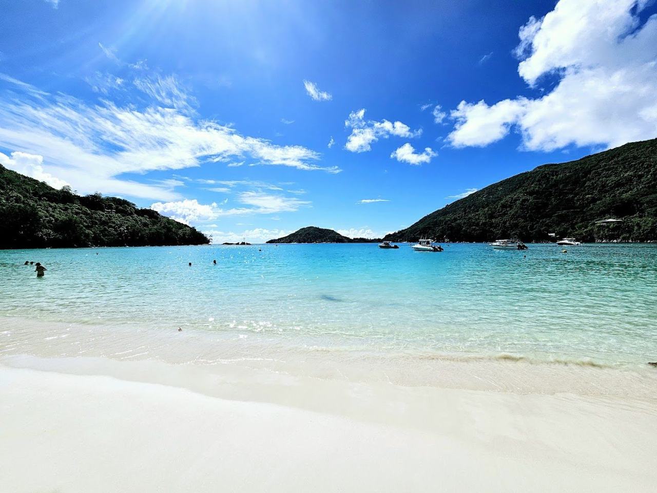 Still glassy water and forested hills behind Port Launay beach on Mahe in the Seychelles