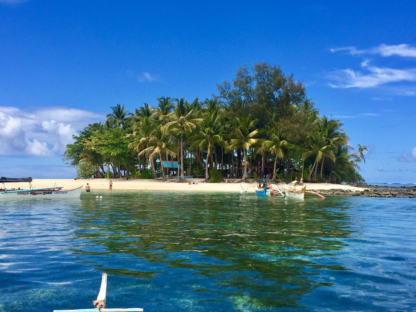 A tiny palm topped islet ringed by empty clear water off the coast of Siargao